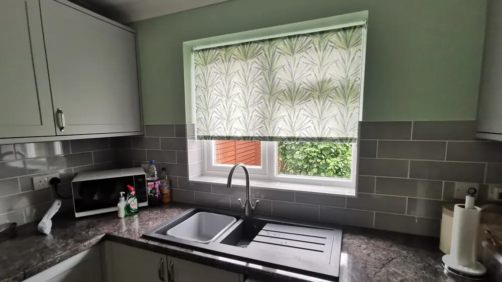 Green leafy patterned roller blind fitted above a kitchen sink, adding colour and personality to the room