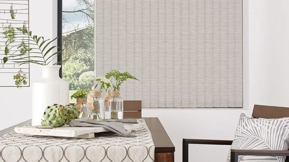 Neutral textured vertical blinds in a bright dining room with a garden view