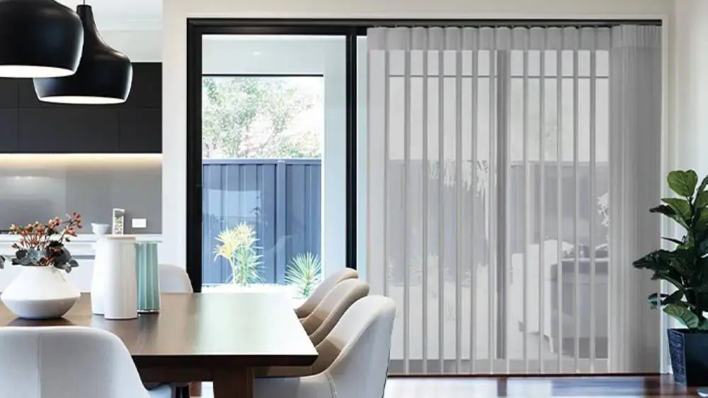 Sheer grey Allusion blinds on bi-fold doors in a modern dining room, filtering soft light through flowing fabric vanes