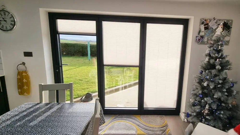 Dark brown INTU pleated blinds fitted into individual panels of bi-fold doors in an open-plan kitchen and living area