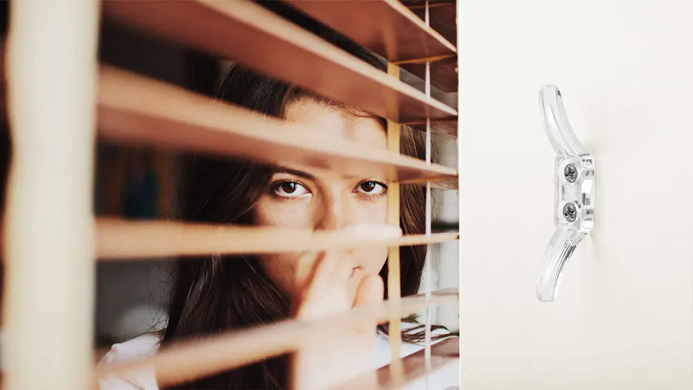 Close-up of a cord cleat mounted on a wall beside a window blind — a simple device that keeps cords taut and out of children's reach