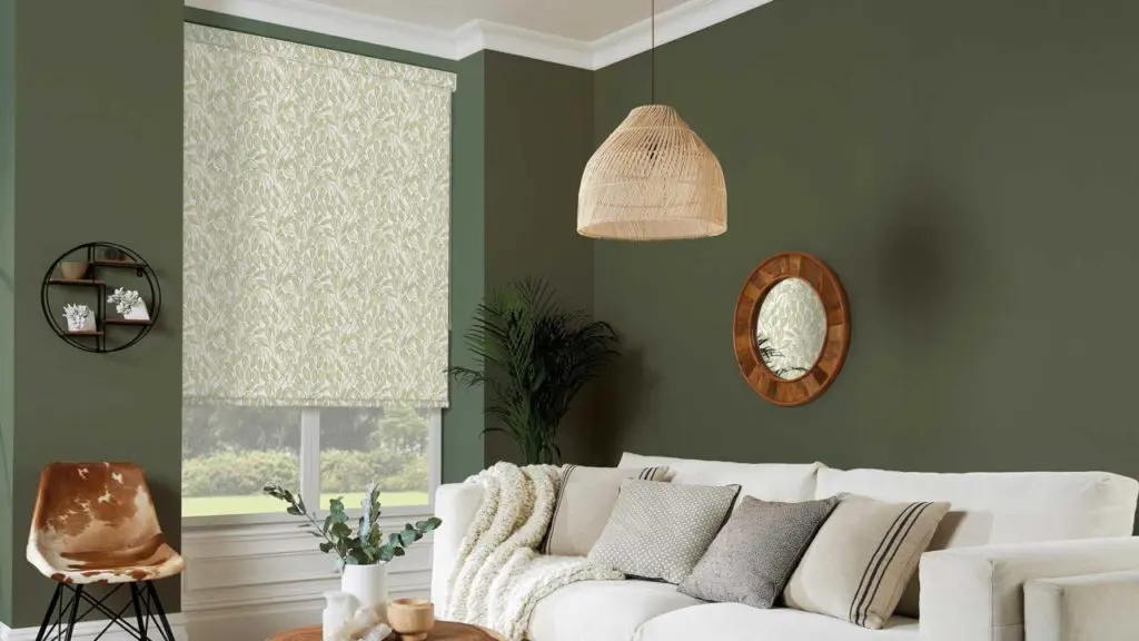 A leafy patterned roller blind with pelmet in a stylish living room with olive green walls and natural furnishings