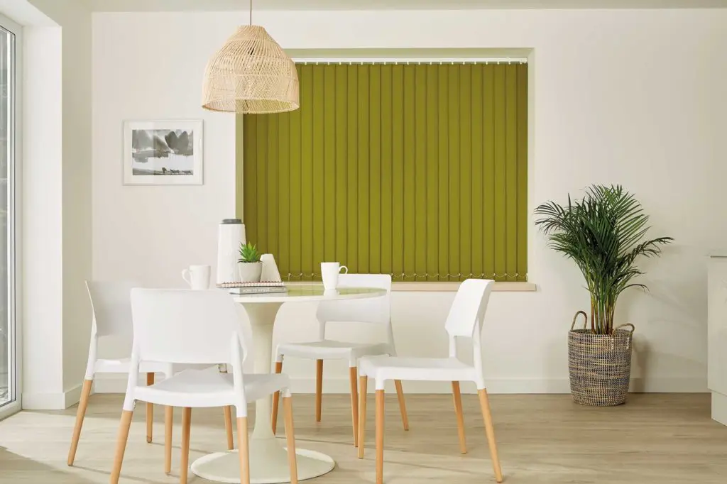 Bold olive green vertical blinds in a bright, contemporary dining room with white furniture and a wicker pendant light